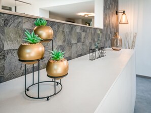 A reception area with a marble wall, a modern light fixture, and three gold-colored planters with green plants. - Comfort Near Historic Huy (Marchin)
