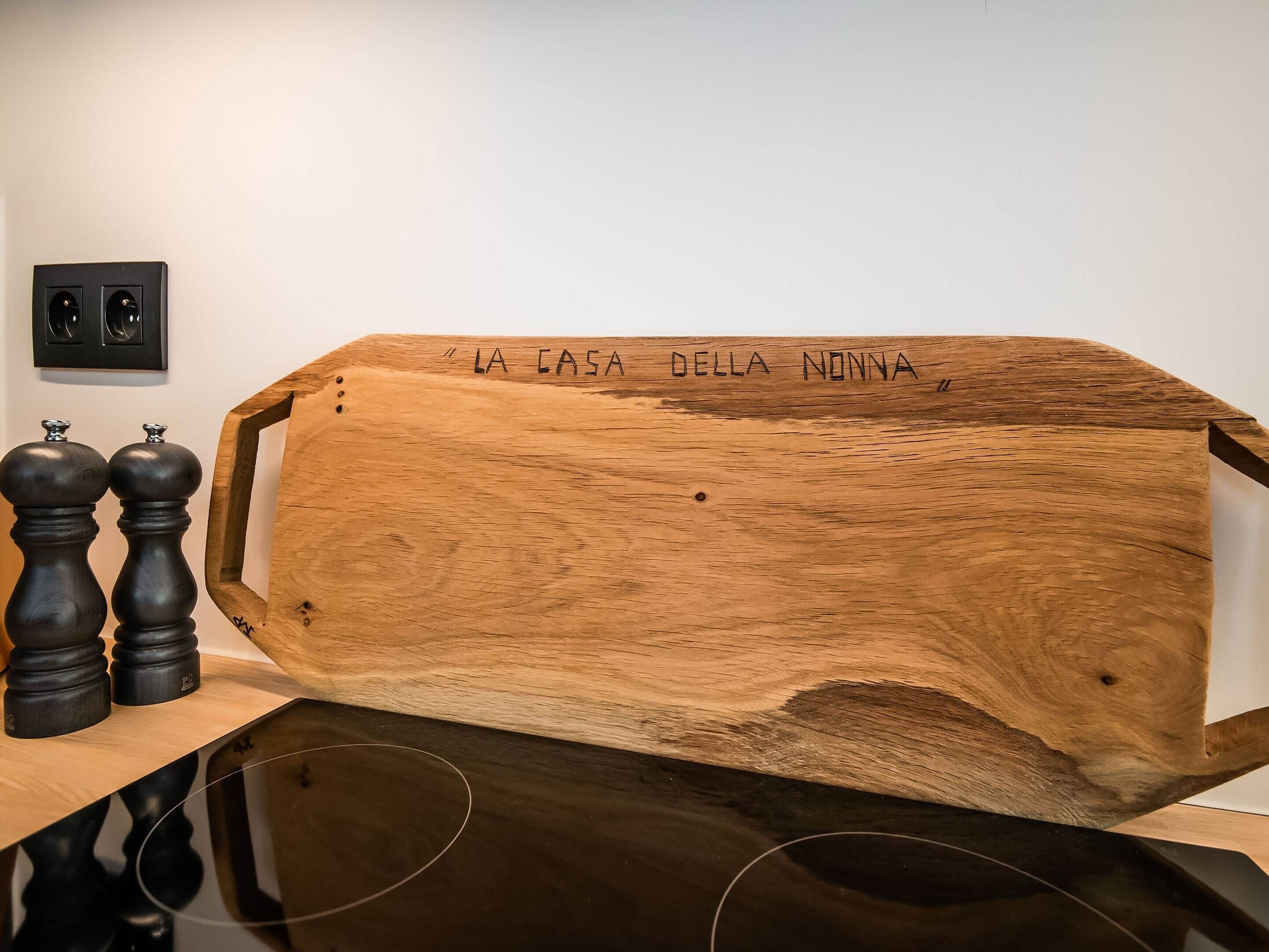 A wooden structure with 'LA CASA DELLA NONNA' carved on it, two black pepper mills, and a framed picture on the wall.
