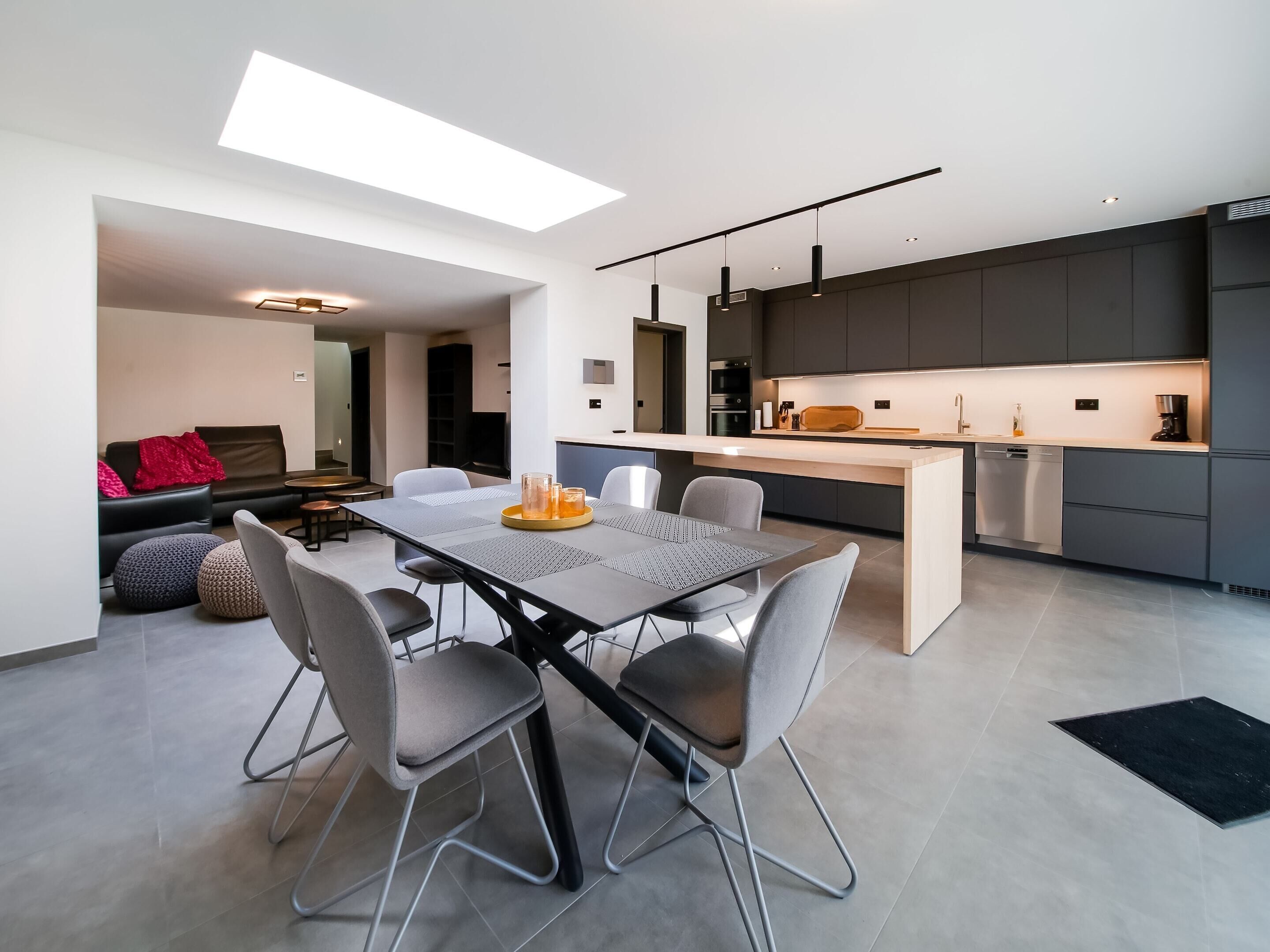 A modern kitchen with a central island, dark cabinetry, and a dining area with a table and chairs.