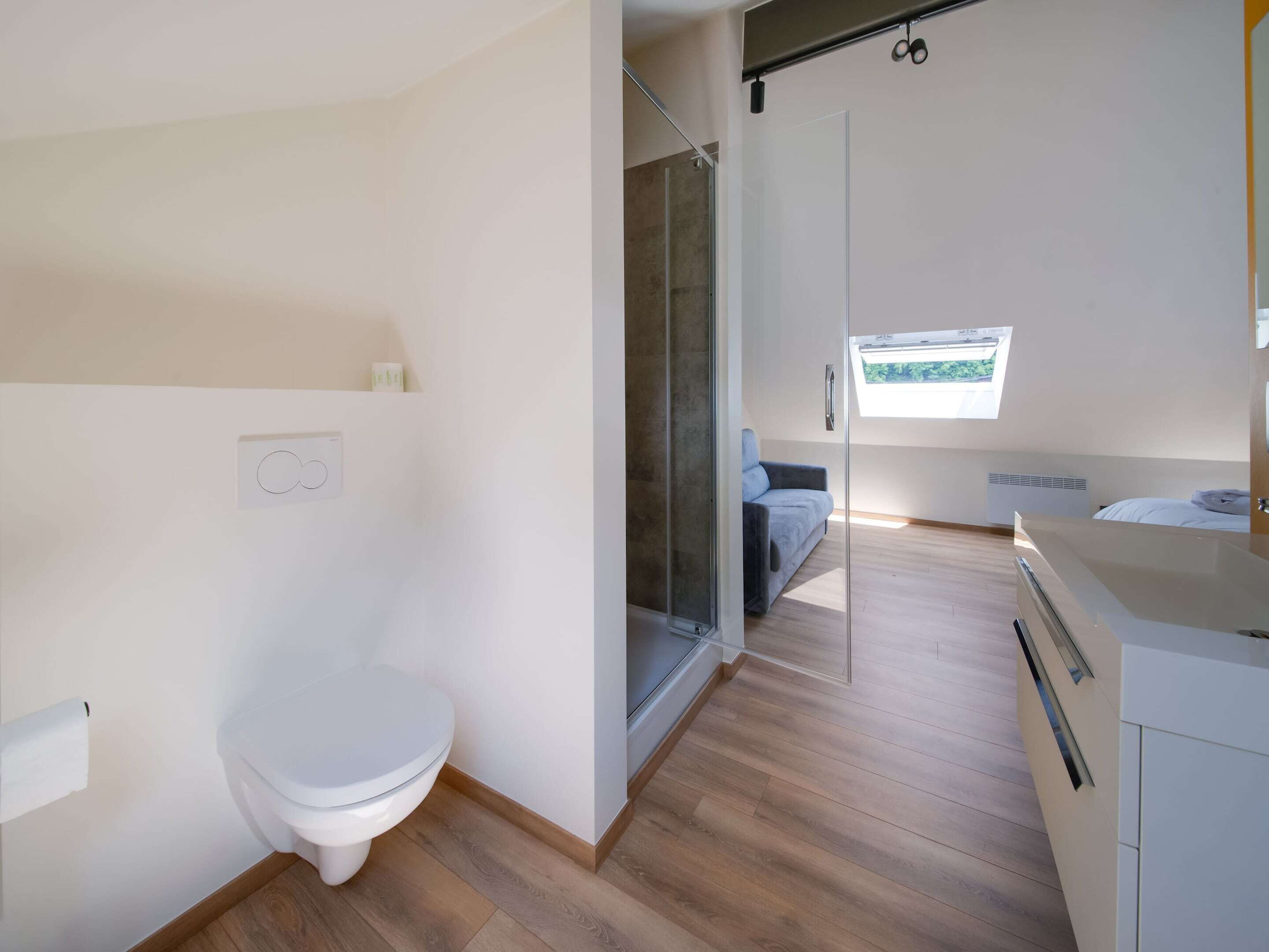 Ein modernes Badezimmer mit Toilette, Dusche und einer Glastür zum Schlafzimmer.