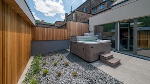 En modern uteplats med ett trädäck, ett bubbelbad och en trädgård med småsten.