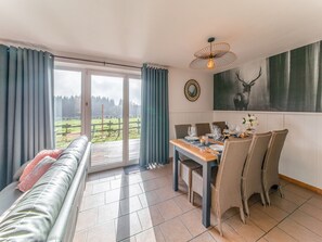 Uma sala de jantar com uma mesa posta para quatro pessoas, um sofá e uma grande janela com cortinas.