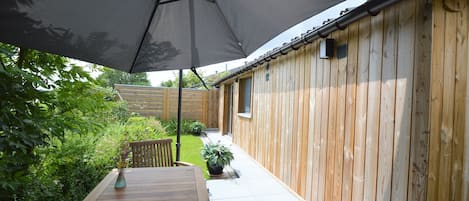 An outdoor patio area with a wooden table and chairs, a large umbrella, and a wooden fence.