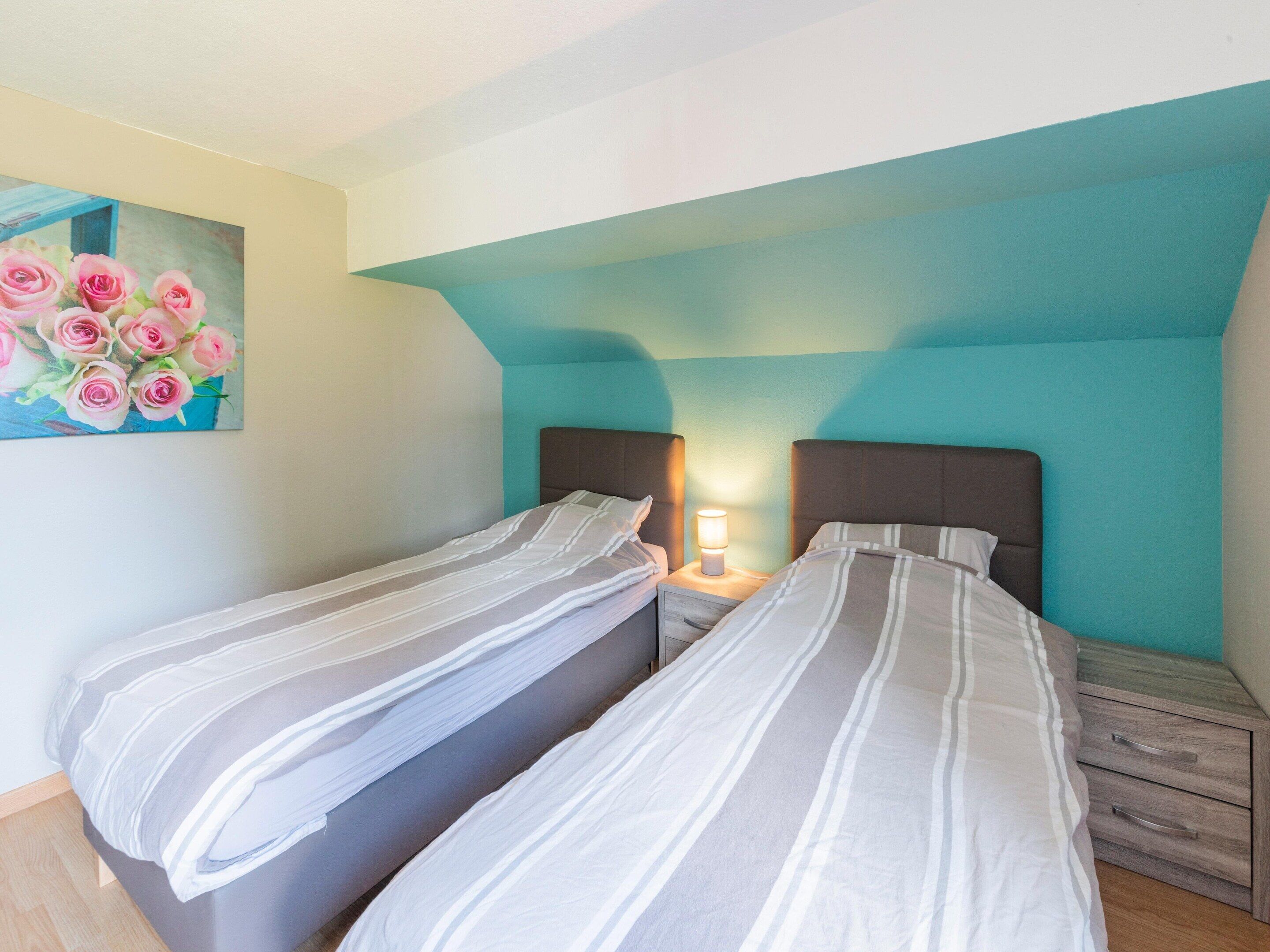 Ein Schlafzimmer mit zwei Einzelbetten, einem Nachttisch mit Lampe und einem Bild von rosa Rosen an der Wand.