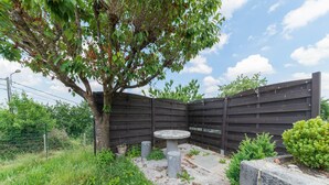 A fenced outdoor area with a table and chairs, surrounded by greenery and a tree. - Holiday Home in Marche-en-famenne With Garden (Marche-en-Famenne)