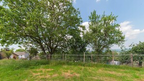A fenced outdoor area with grass and trees, a house in the background, and a clear sky. - Holiday Home in Marche-en-famenne With Garden (Marche-en-Famenne)