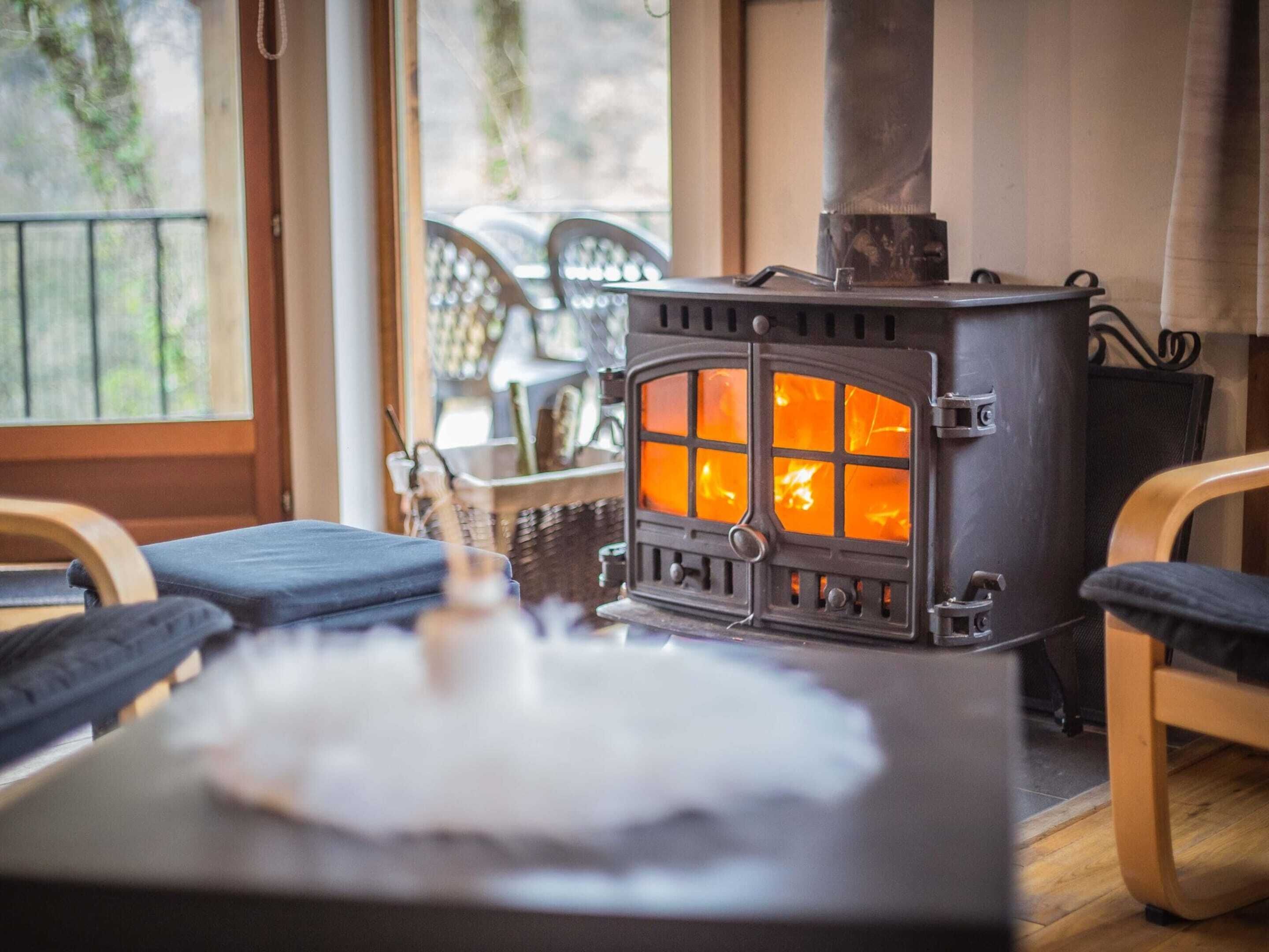 A cozy room with a wood-burning stove, a table with a white placemat, and wooden chairs.