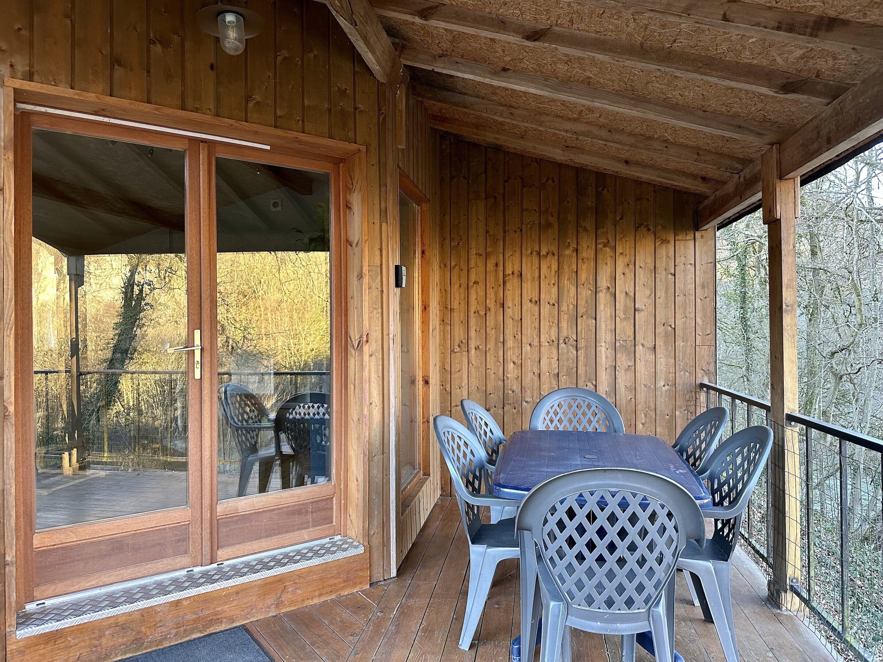 A wooden deck with a table and chairs, a sliding glass door, and a view of trees.