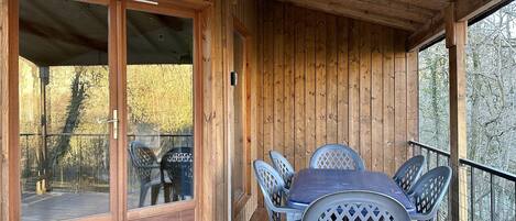 A wooden deck with a table and chairs, a sliding glass door, and a view of trees.
