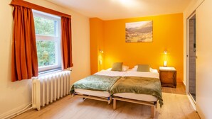 Ein Schlafzimmer mit zwei Betten, einem Fenster mit Vorhängen, einem Heizkörper und einem Bild an der Wand.