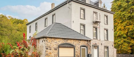 A two-story stone building with a gabled roof, a small stone extension with a garage door, and a wooden front porch.