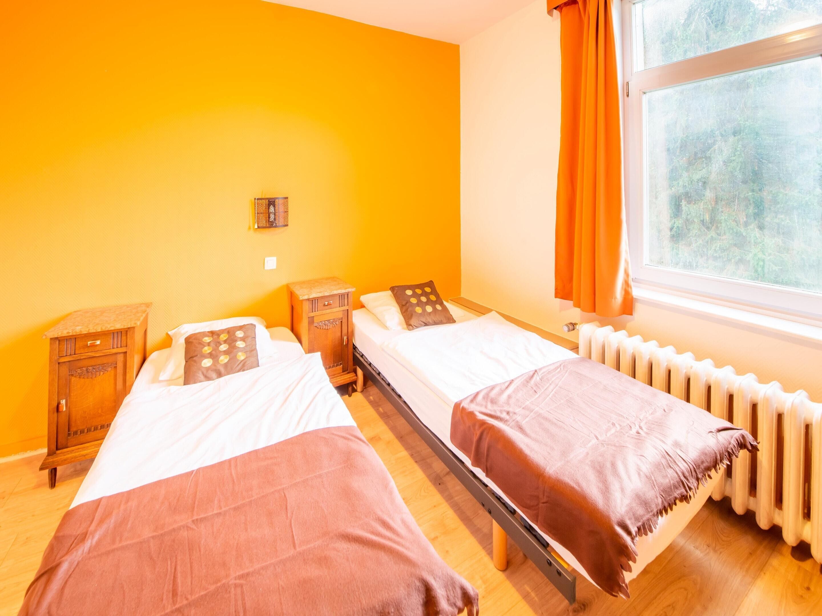 A room with two beds, a radiator, a window with curtains, and a small cabinet.