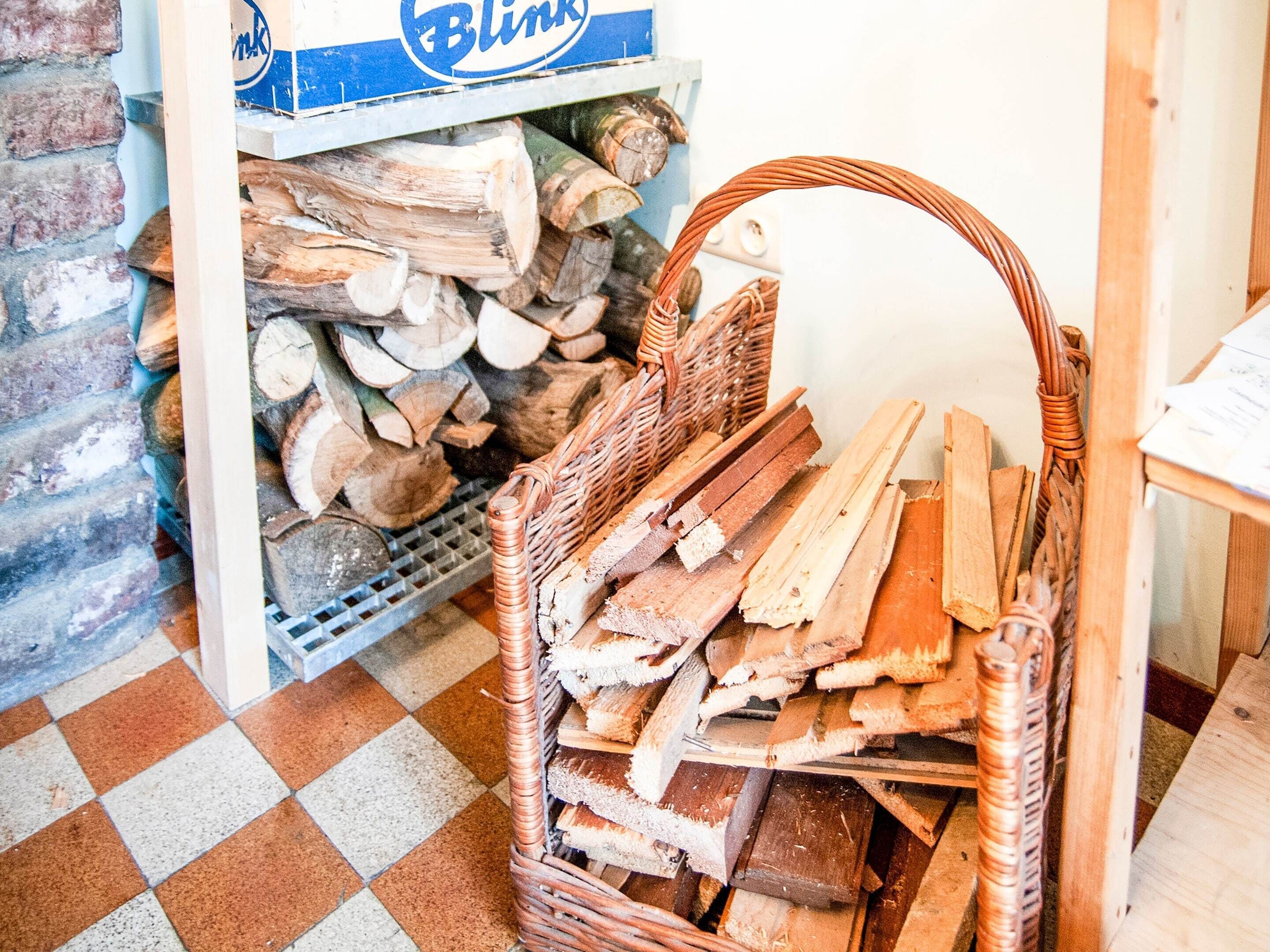 A room with a wicker basket filled with firewood, a shelf with neatly stacked logs, and a checkered floor.