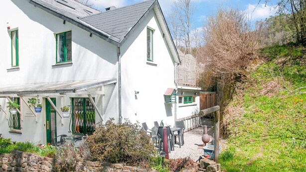 A white building with a sloped roof, a stone wall, and a gravel path leading to a seating area with tables and chairs. - Cozy Country Stay, Stoumont (Stoumont)