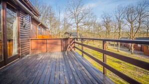 Une terrasse en bois avec une rambarde, une cabane et, au loin, une vue sur des arbres sans feuilles.