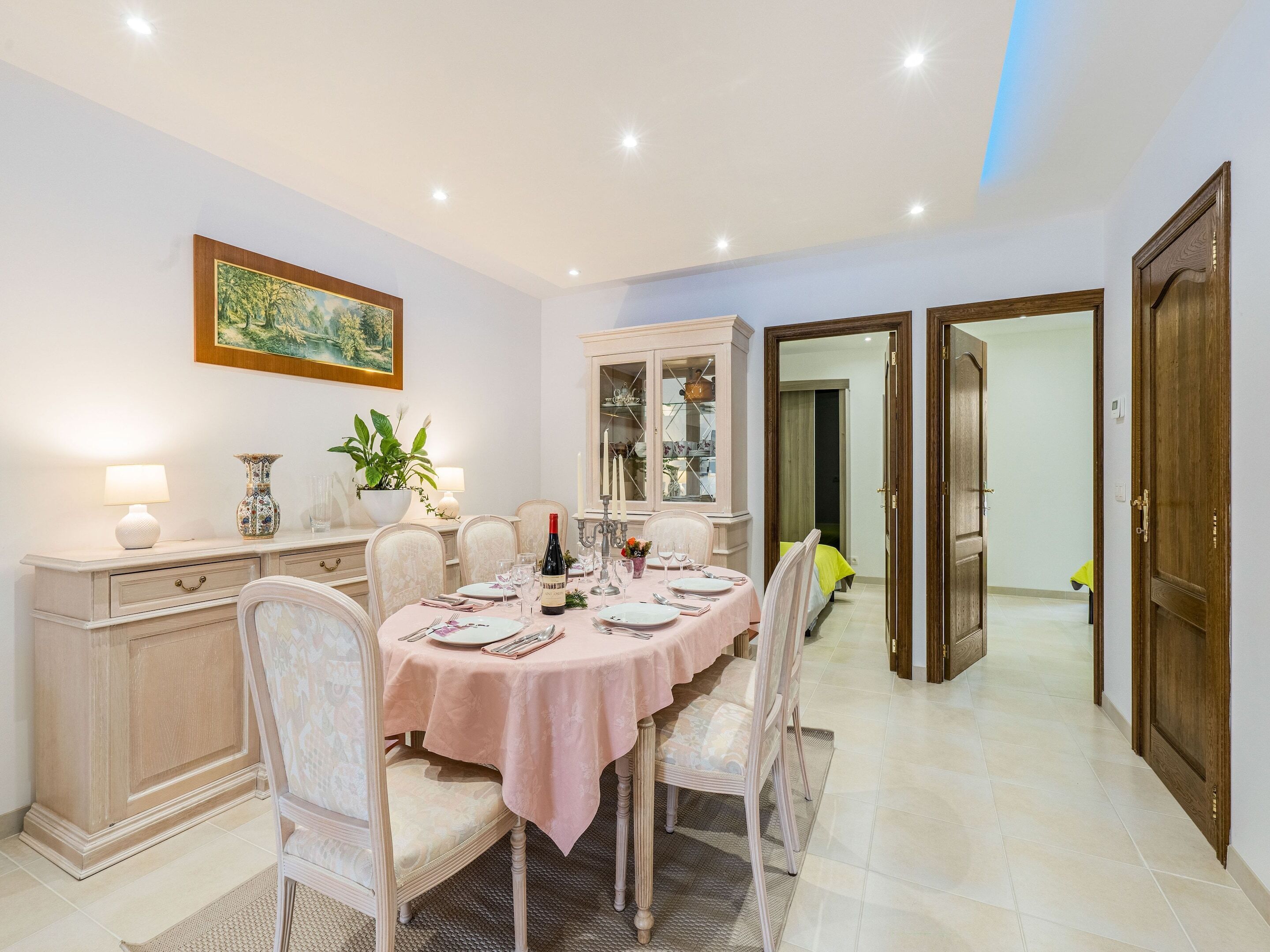 A dining area with a round table, chairs, a cabinet, and a painting on the wall.
