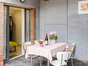 Una mesa dispuesta con una botella de vino, una copa y un arreglo floral, rodeada de sillas.