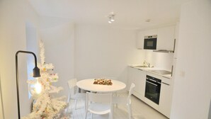 A modern kitchen with white cabinets, a built-in oven, and a dining area with a white table and chairs. - Apartment in Durbuy Near Adventure Park (Durbuy)