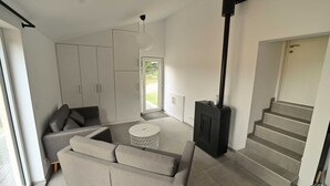 A modern living room with a grey sofa, a white coffee table, and a black fireplace. There is a staircase leading to an upper level. - Bungalow by Lake Rabais in Virton (Virton)