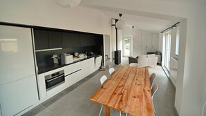 A modern kitchen with white cabinets, a wooden dining table, and a large window providing natural light. - Bungalow by Lake Rabais in Virton (Virton)