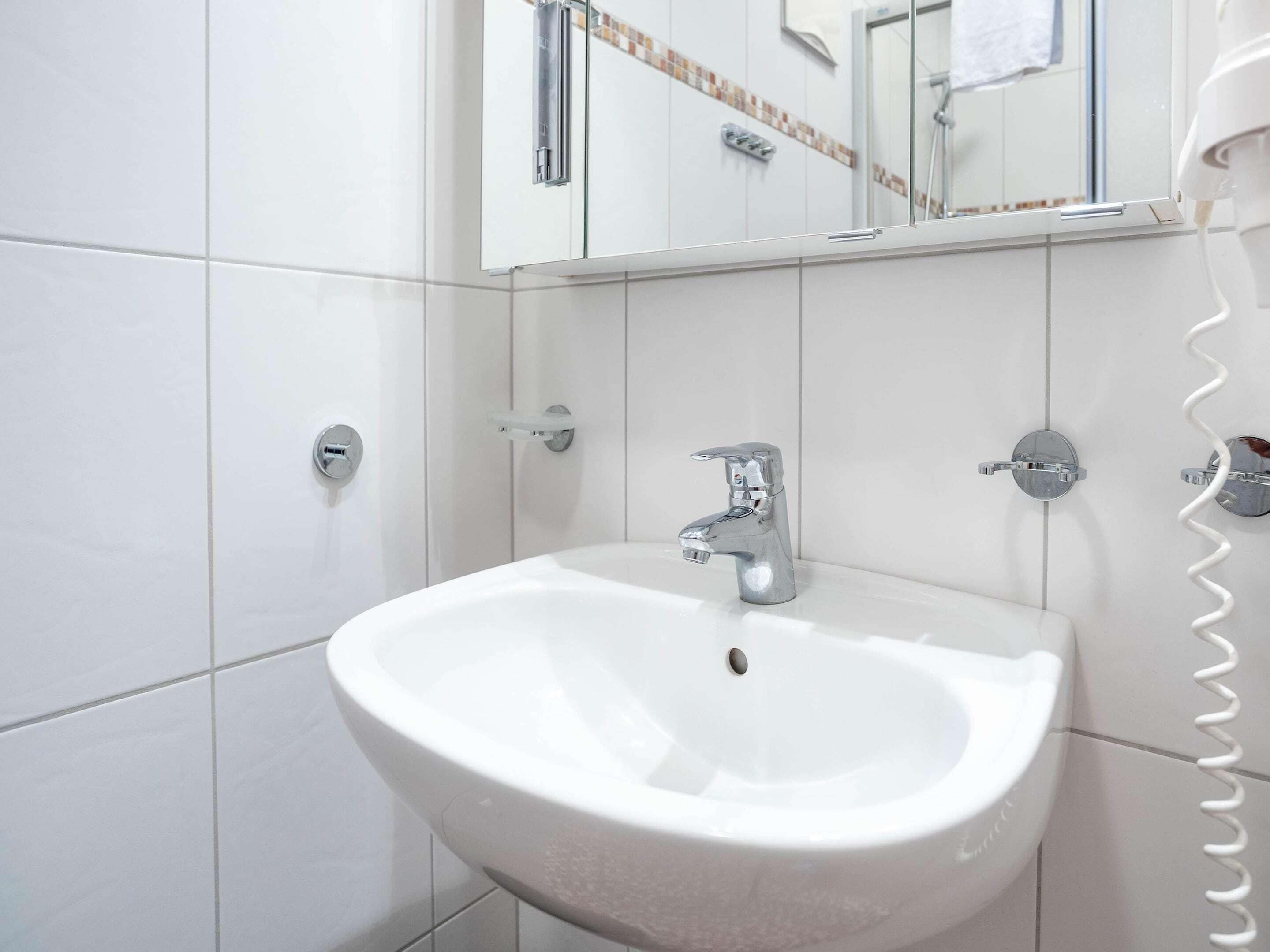 Une salle de bain avec un lavabo blanc, un robinet chromé et un miroir au-dessus.