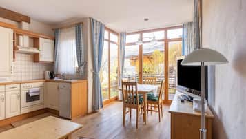 Una cocina con armarios de madera, un comedor con mesa y sillas, un televisor y un amplio ventanal con cortinas.