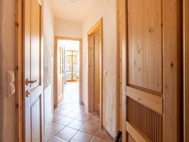 Un pasillo con puertas de madera y suelo de baldosas que conduce a un espacio abierto con vistas.