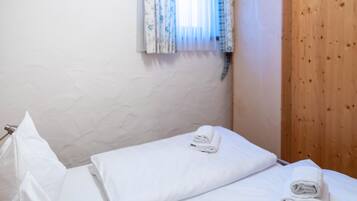 Una habitación pequeña y limpia, con una cama individual, cabecero de madera y una ventana con cortinas traslúcidas.