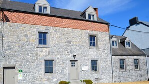 Un edificio de piedra con una puerta gris, varias ventanas y un pequeño jardín con grava y arbustos.