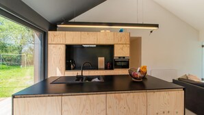 A modern kitchen with wooden cabinetry, a black countertop, and a built-in oven. - Charming Home With Sauna (Paliseul)