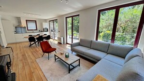 A modern living space with a dining area, kitchen, and large windows offering a view of greenery. - Villa in Durbuy With Jacuzzi & Golf Access (Durbuy)