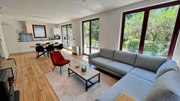 A modern living space with a dining area, kitchen, and large windows offering a view of greenery. - Villa in Durbuy With Jacuzzi & Golf Access (Durbuy)