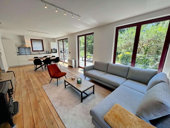 Ein moderner Wohnraum mit Essbereich, Küche und großen Fenstern mit Blick auf Grünflächen.