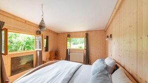A wooden room with a bed, a window, a painting, and a hanging light fixture. - Holiday Home in Bievre With Garden (Bievre)