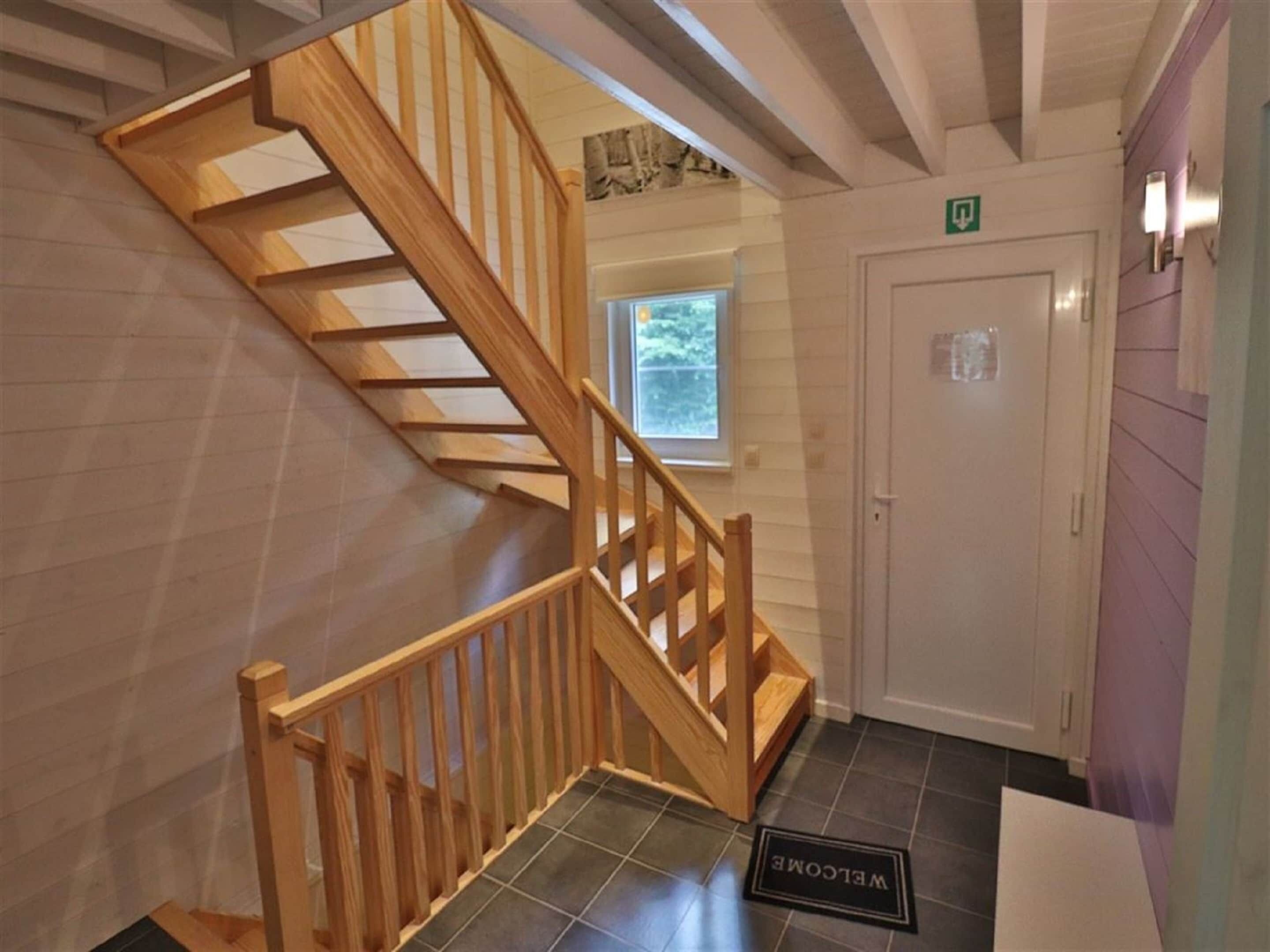 Una escalera de madera que conduce a un rellano con una puerta marcada 'P' y un ventanal encima.