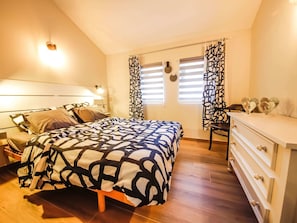 Ein Schlafzimmer mit Bett, Nachttischen, einem Schminktisch und einem Fenster mit Vorhängen.
