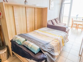 Un dormitorio con un armario de madera, una cama con ropa de cama estampada, un sofá y vistas a través de una ventana.
