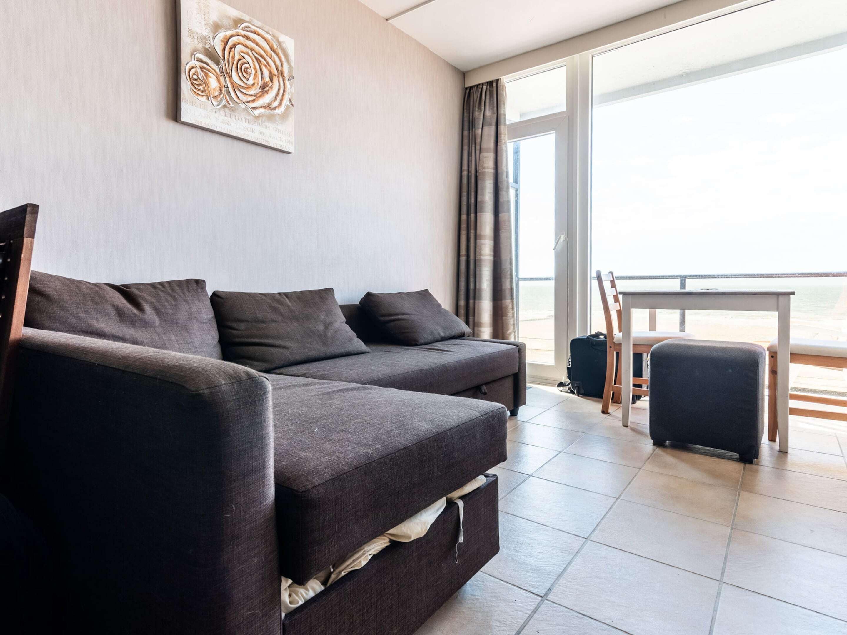 A modern living room with a sofa, a small table, and a view of the sea through large windows.