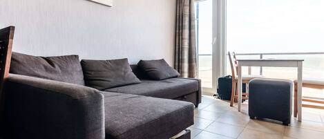 A modern living room with a sofa, a small table, and a view of the sea through large windows.