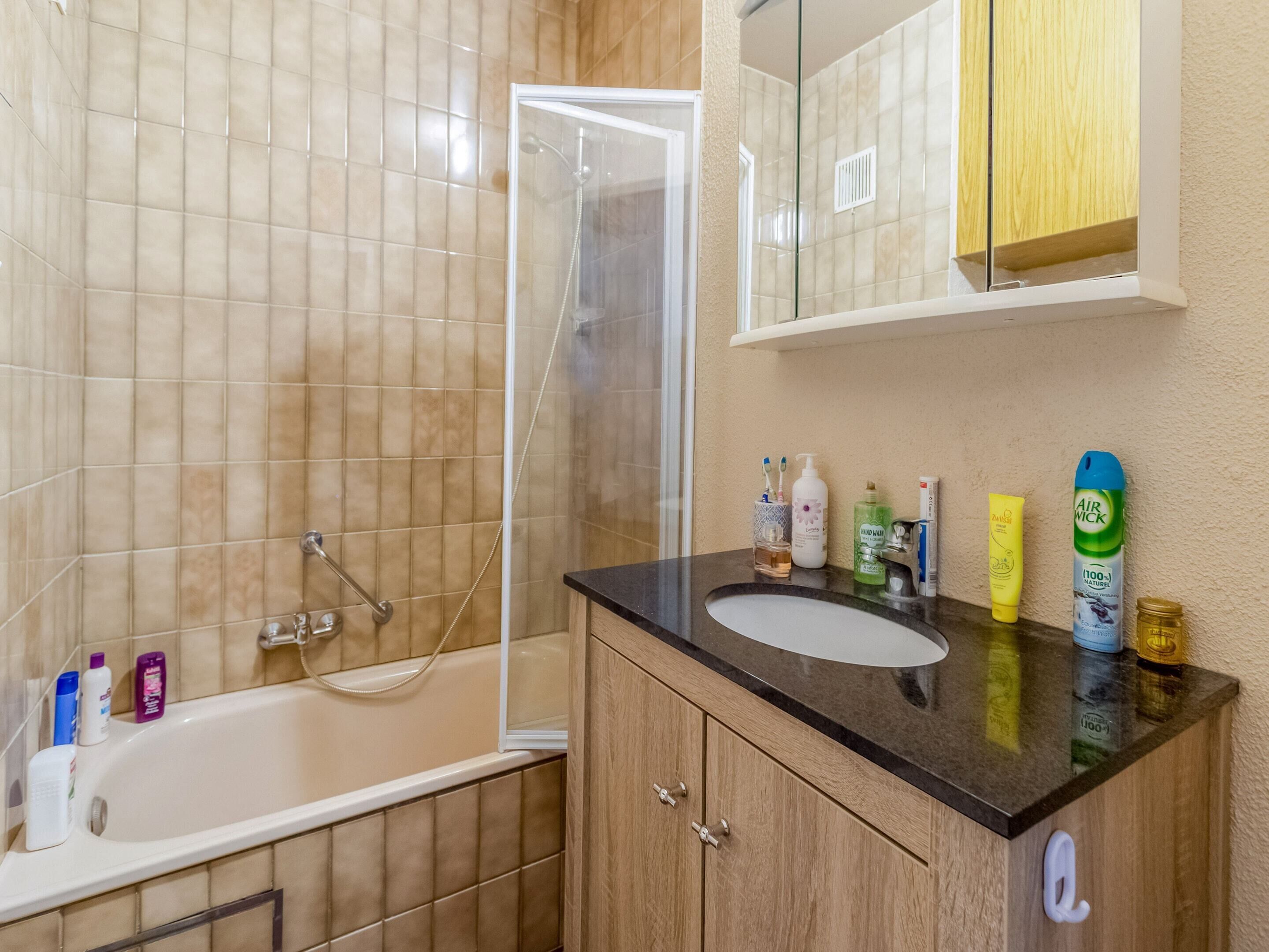 A bathroom with a bathtub, a shower, a sink, and toiletries on the countertop.