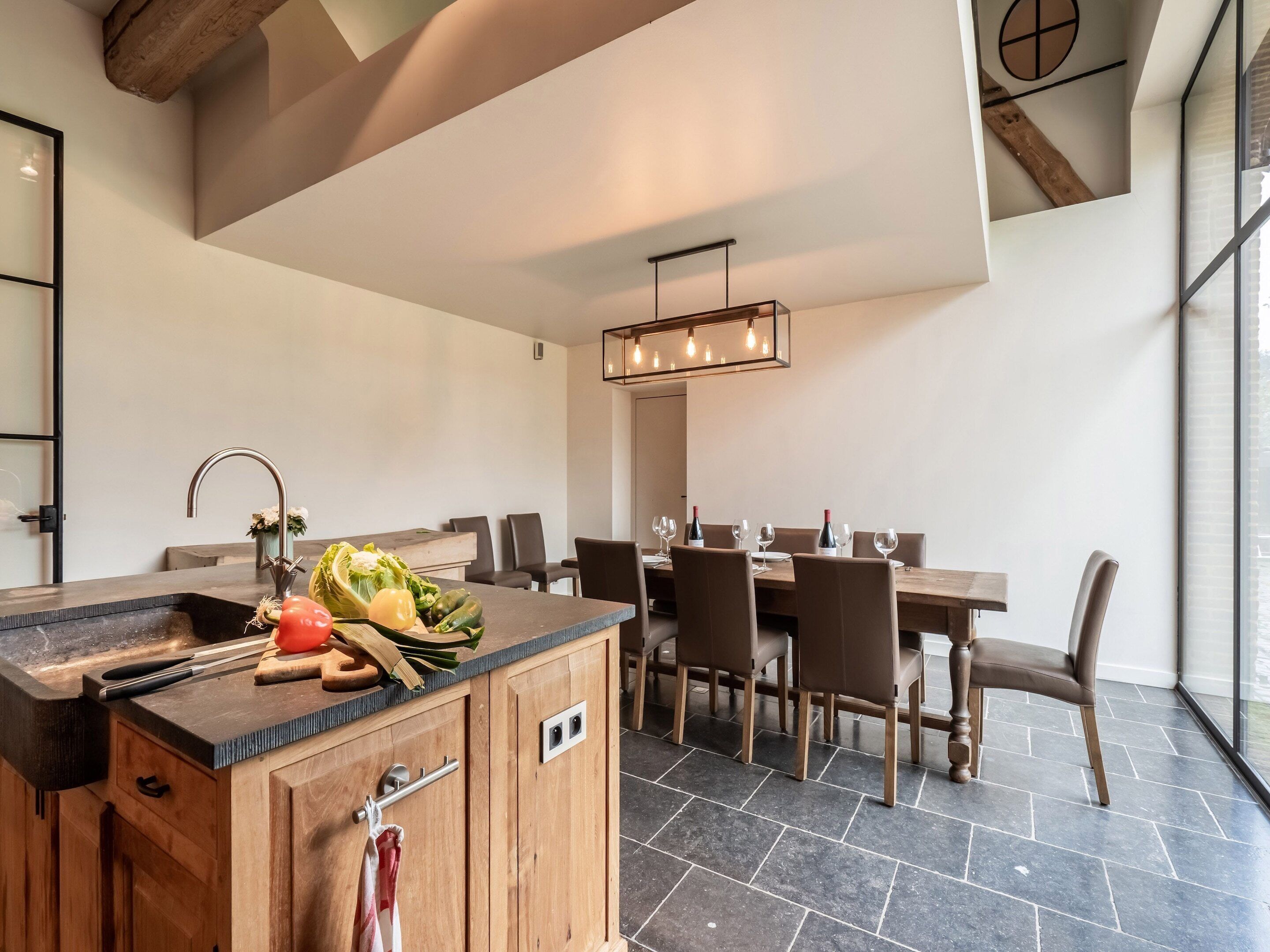 Una cocina moderna con una isla de madera, un comedor con sillas y un ventanal grande.