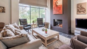 A modern living room with a fireplace, comfortable seating, and large windows offering a view of the outdoors. - Beernem Countryside Home (Beernem)