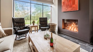 A modern living room with a fireplace, leather chairs, a wooden coffee table with champagne, and a large window offering a view of the outdoors. - Beernem Countryside Home (Beernem)