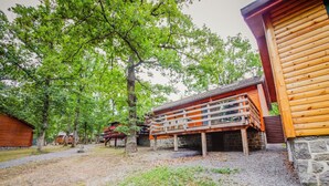 A rustic cabin with a wooden deck and stone foundation, surrounded by trees and a gravel path. - Chalet Le Beau Renard, Heure (Somme-Leuze)
