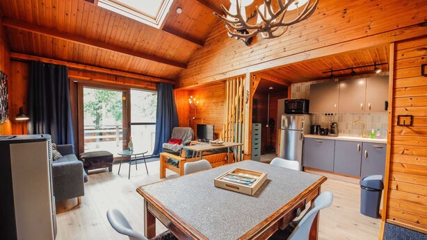 A cozy cabin with a dining area, kitchen, and a large window. - Chalet Le Beau Renard, Heure (Somme-Leuze)