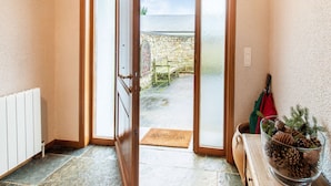 Una stanza con una porta in legno, un termosifone, una porta vetrata che dà sull'esterno, un tappetino e una ciotola di vetro con pigne.