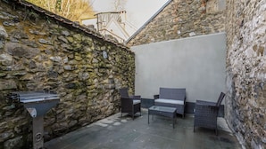 A stone-walled patio with a grill, wicker furniture, and a tiled floor. - Cosy Holiday Home in Hastiere With a Terrace (Hastiere)