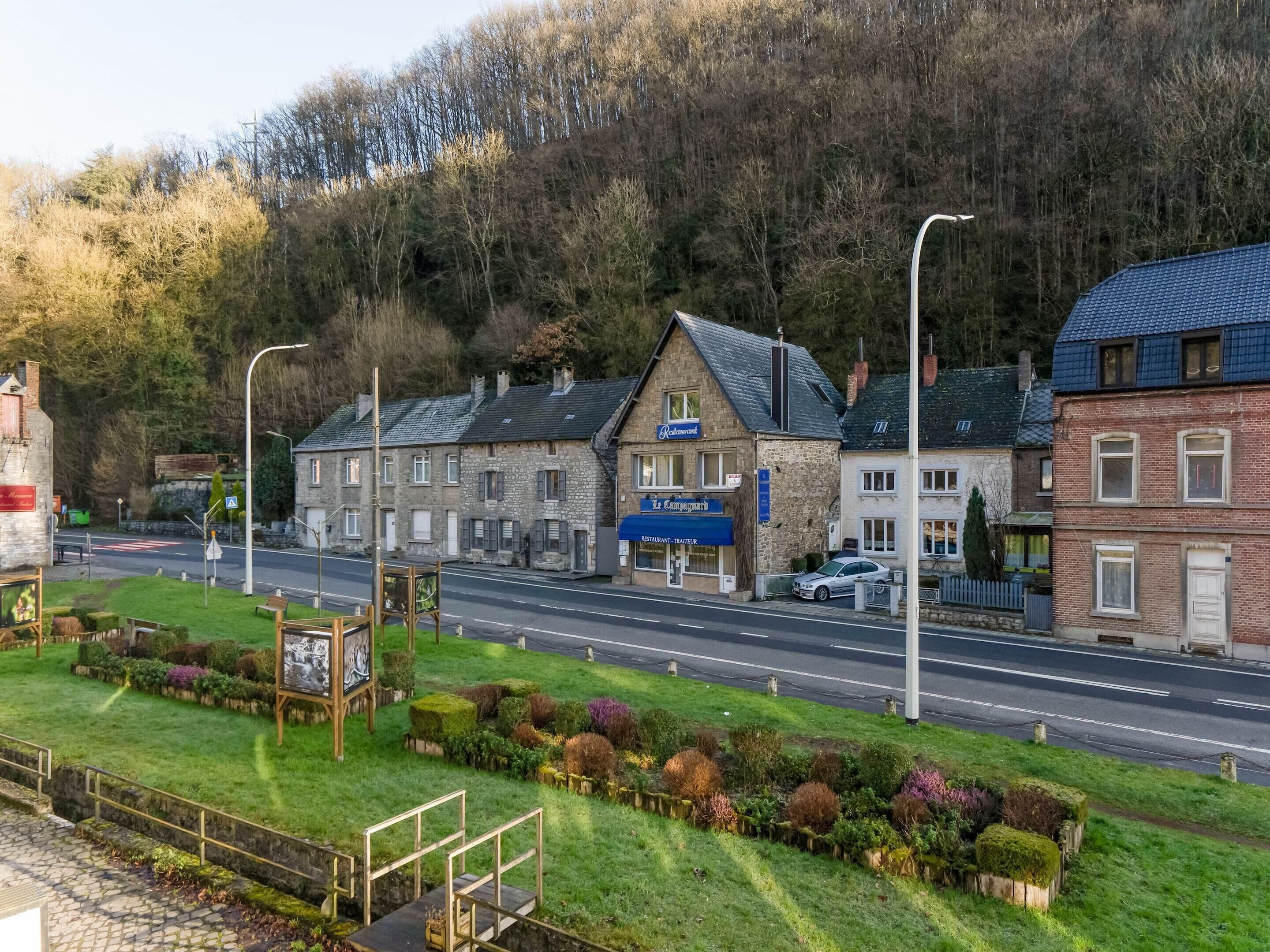 A building with a restaurant sign, a street, and a forested hillside.