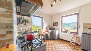 A kitchen with a checkered floor, a red pot on the stove, and a view of the countryside through large windows. - Farmhouse Kalys in Vielsalm With 180° View of the Forest (Vielsalm)