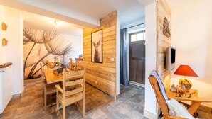 A cozy dining area with a wooden table and chairs, a large framed picture on the wall, and a television mounted on the wall. - Farmhouse Kalys in Vielsalm With 180° View of the Forest (Vielsalm)